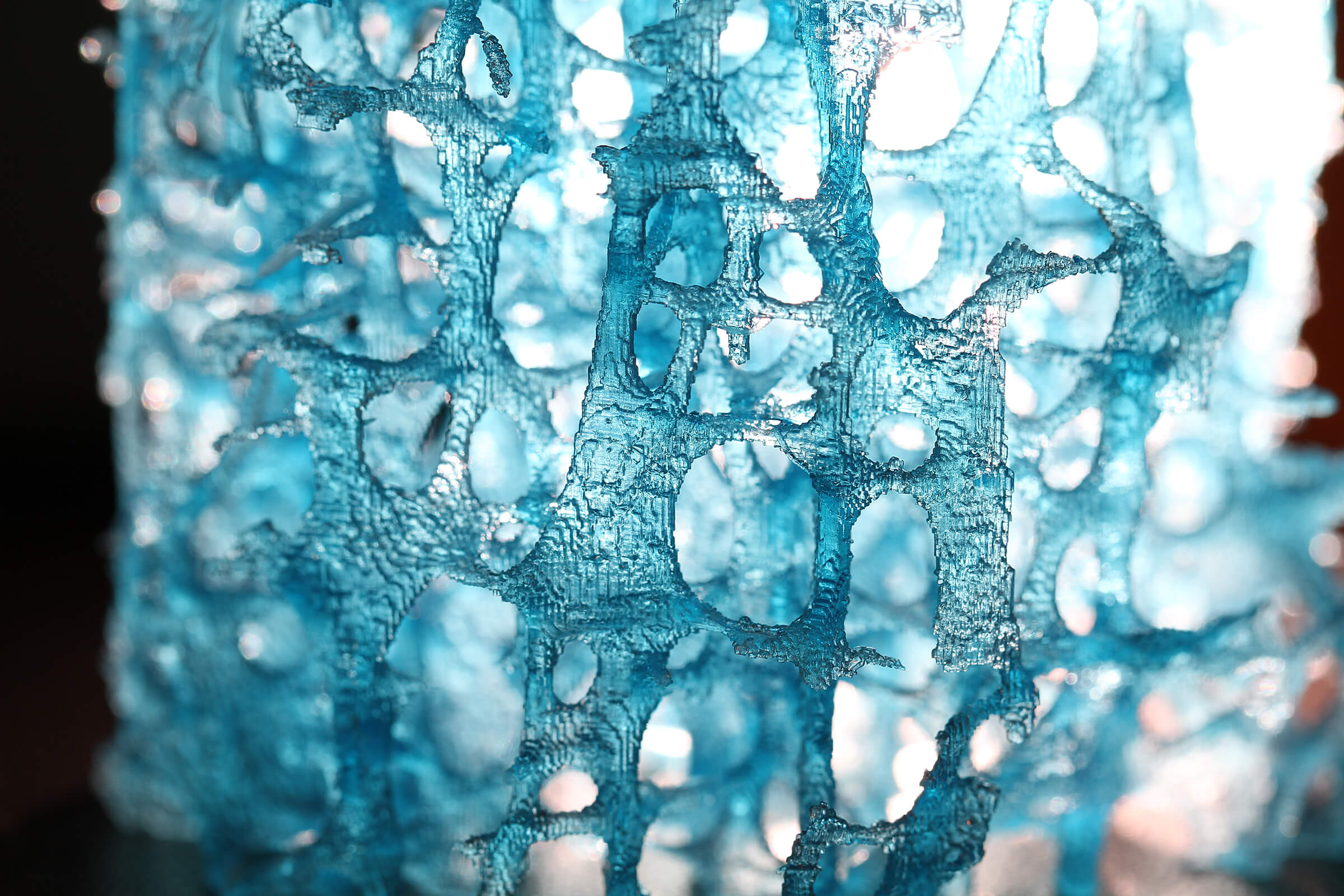 The 3D-printed model of bone's structure is bright blue and has light shining through its porous structure